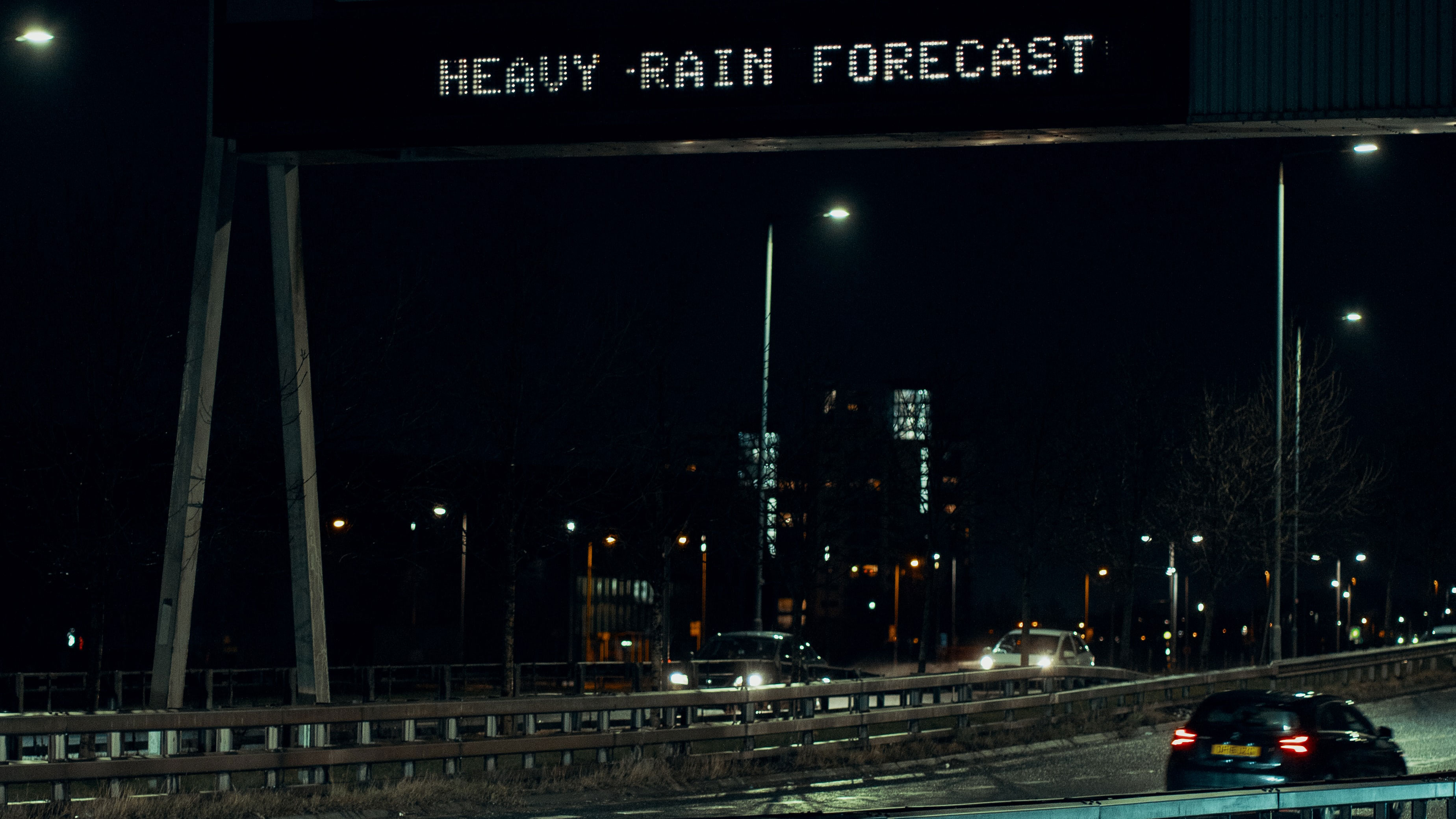 Heavy rain forecast board above city road at night with cars 