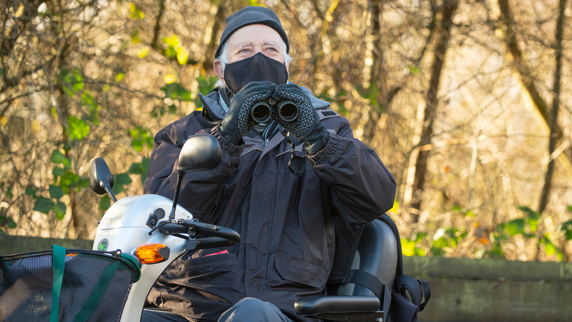 Older man with binoculars on mobility scooter observing birds from a viewing platform at Rye Meads Nature Reserve