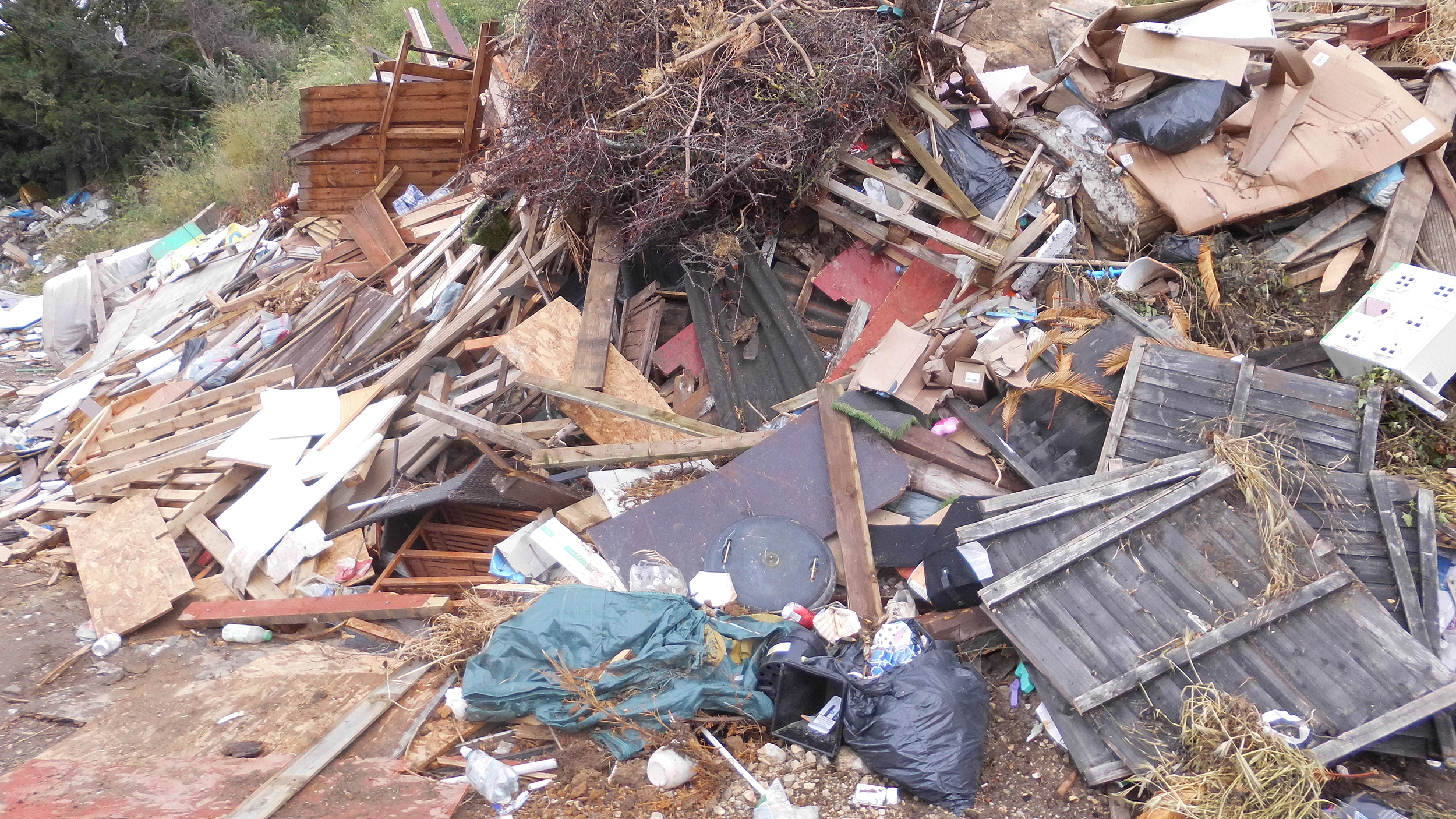 Fly tipping on ground, plastic bags with waste, garden fence panels, waste wood, garden waste