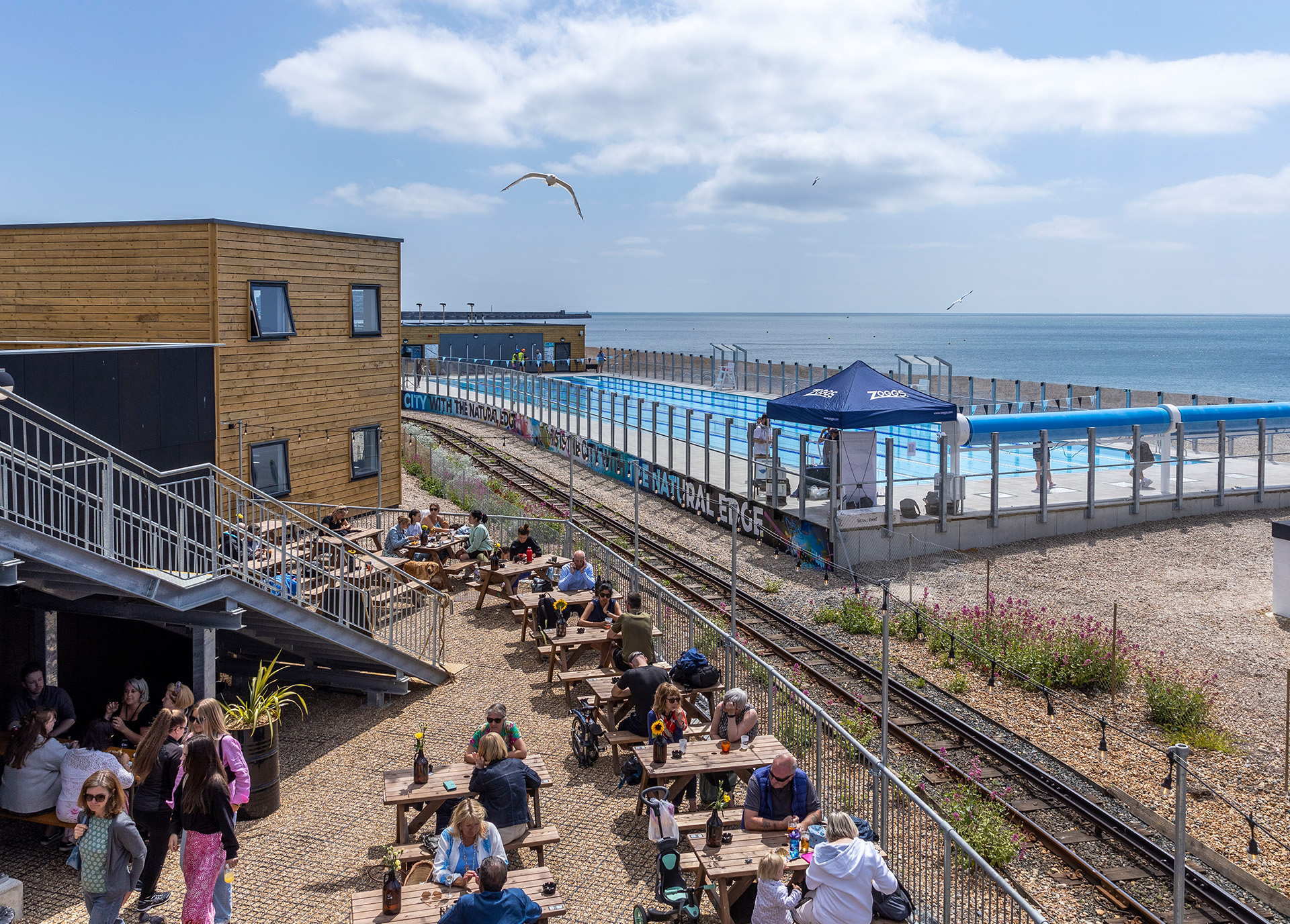 Rail tracks run through the middle of picnic benches on one side and an outdoor pool on the other