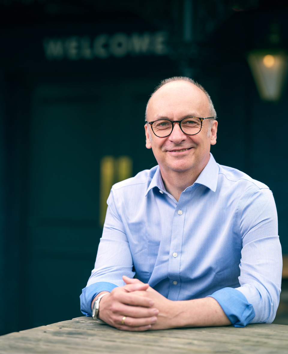 Stephen sat at a wooden table with a welcome sign blurred in the background