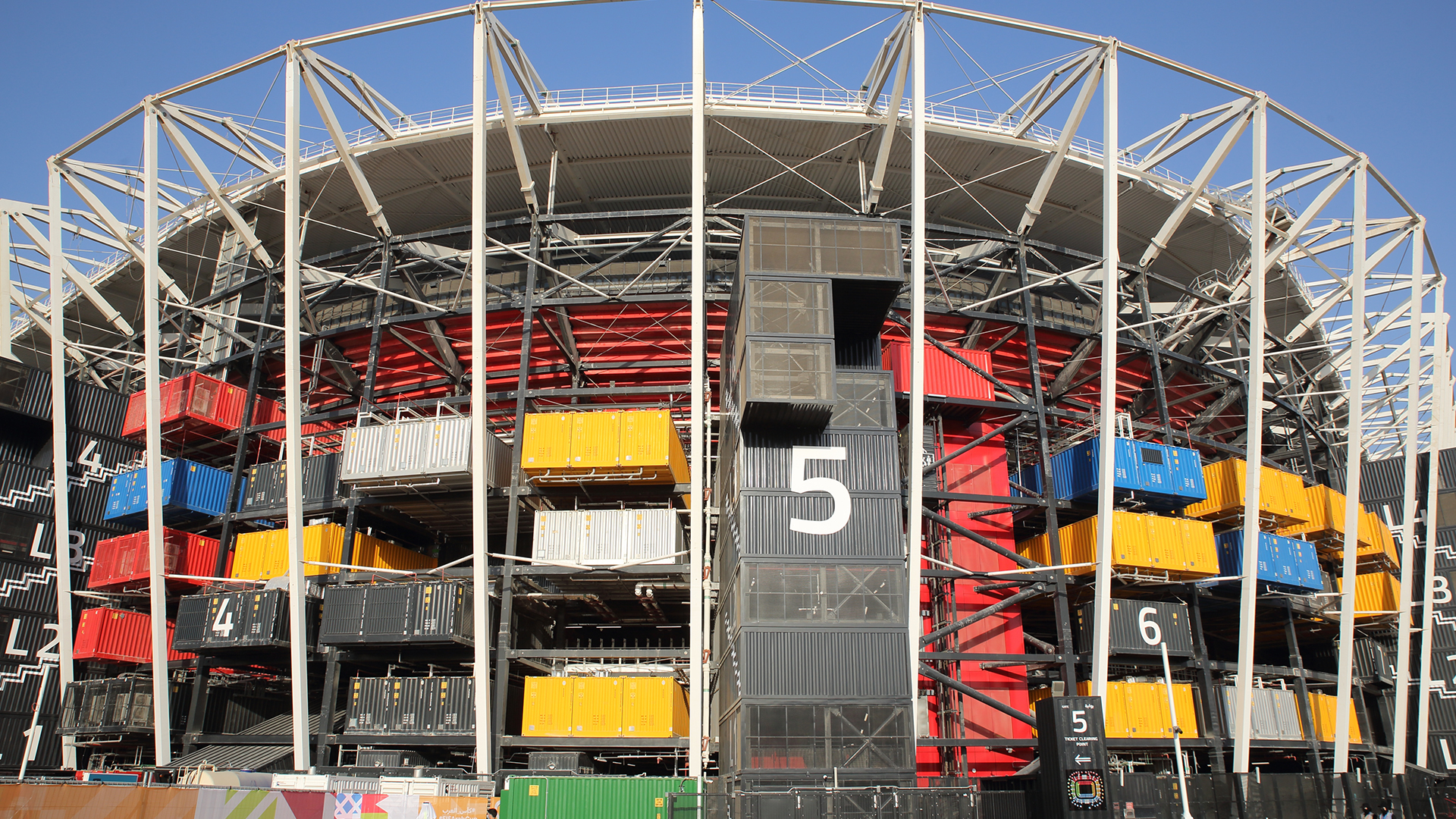 Football stadium made up of shipping containers with water and sail boats in the foreground