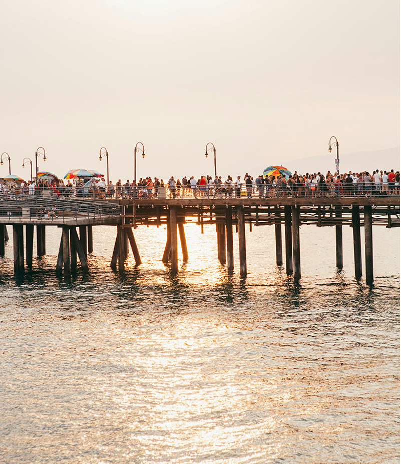 People walking across wooden pier over the sea at sunset