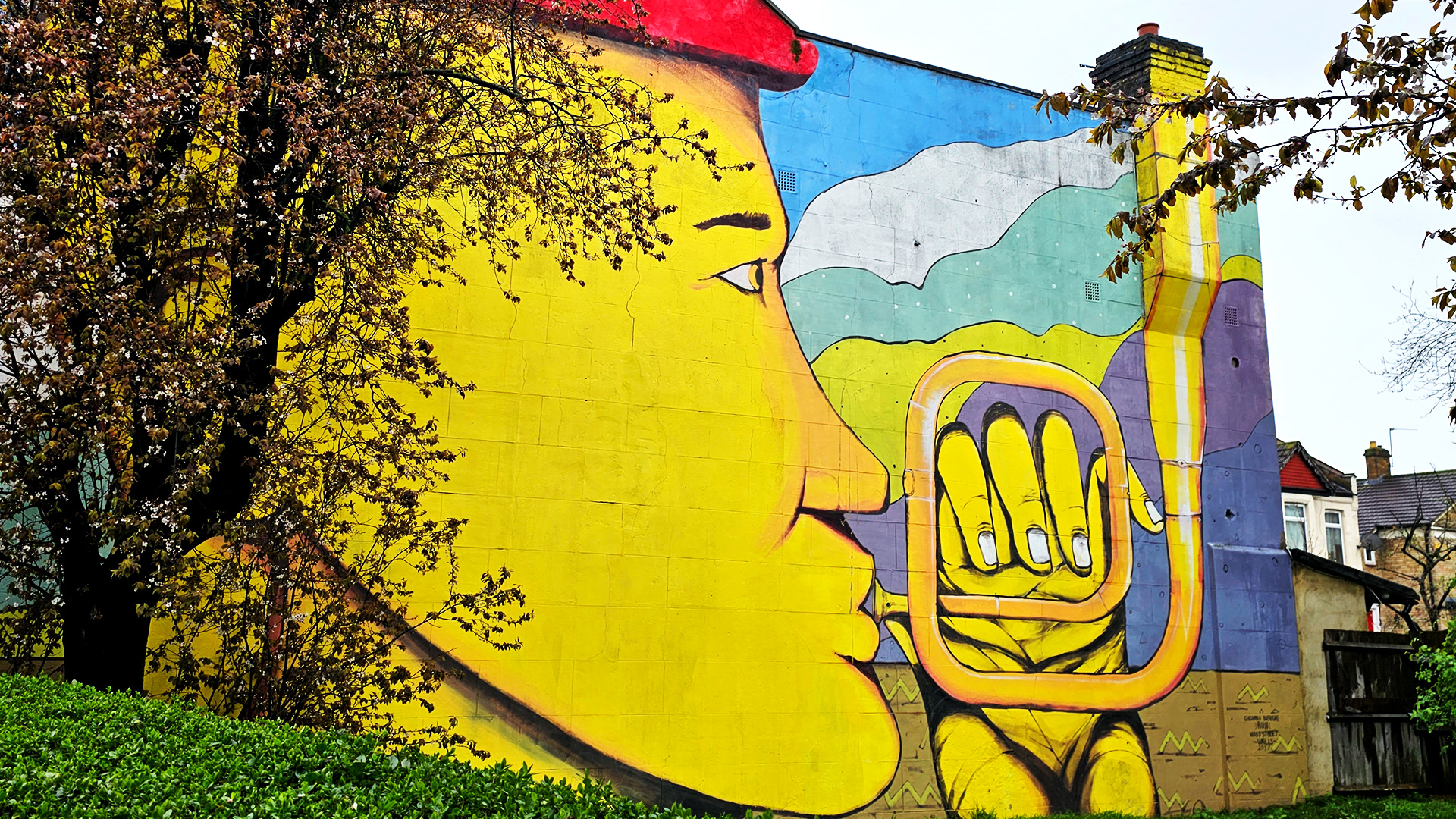 Painting covering the entire side of a building of a yellow person playing a trombone