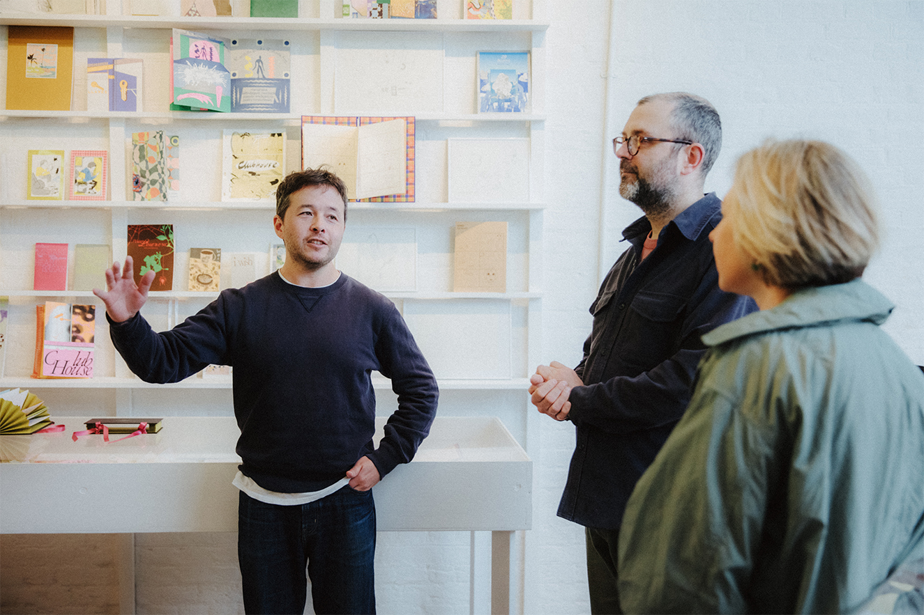 London Centre for Book Arts Yulia speaks with owners Simon and Ira in front of book shelves