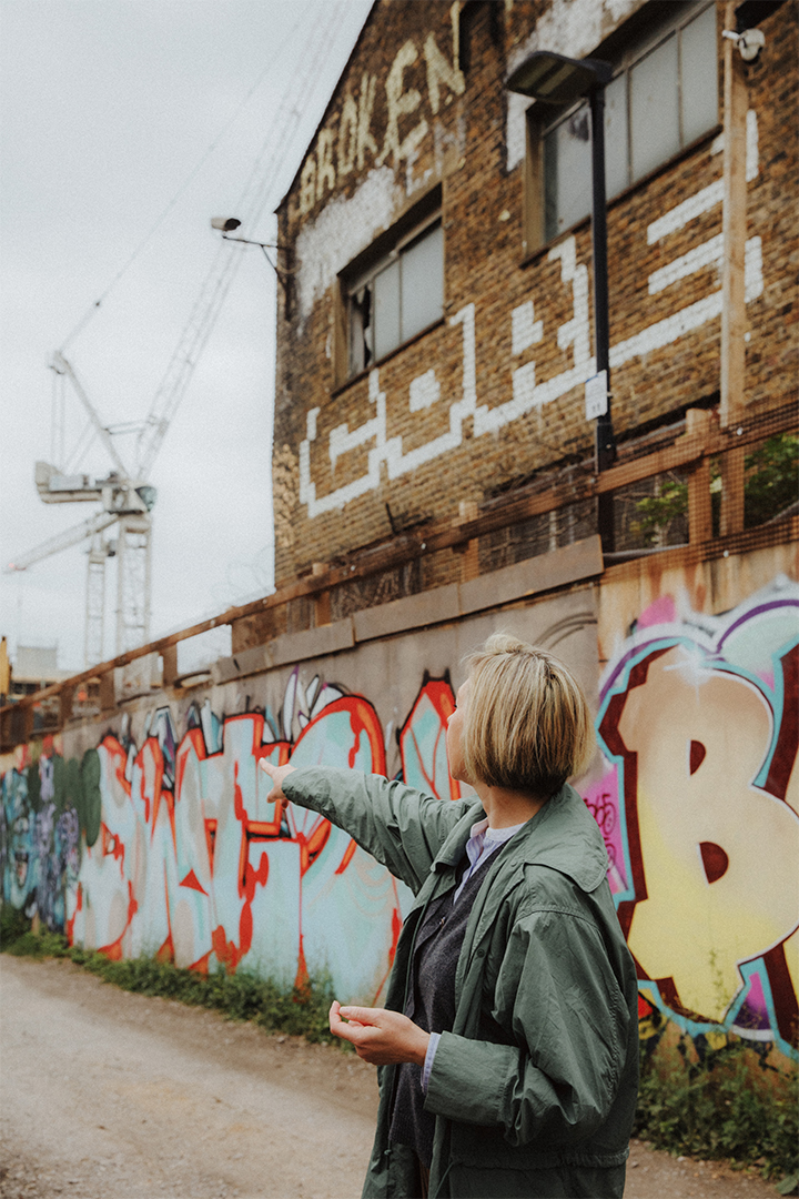 Yulia Pak MRICS Hackney Wick Yulia pointing to a development in Hackney Wick amongst warehosues