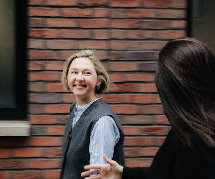 Yulia Pak MRICS Motion blur image of Yulia walking alongside brick wall talking to colleague