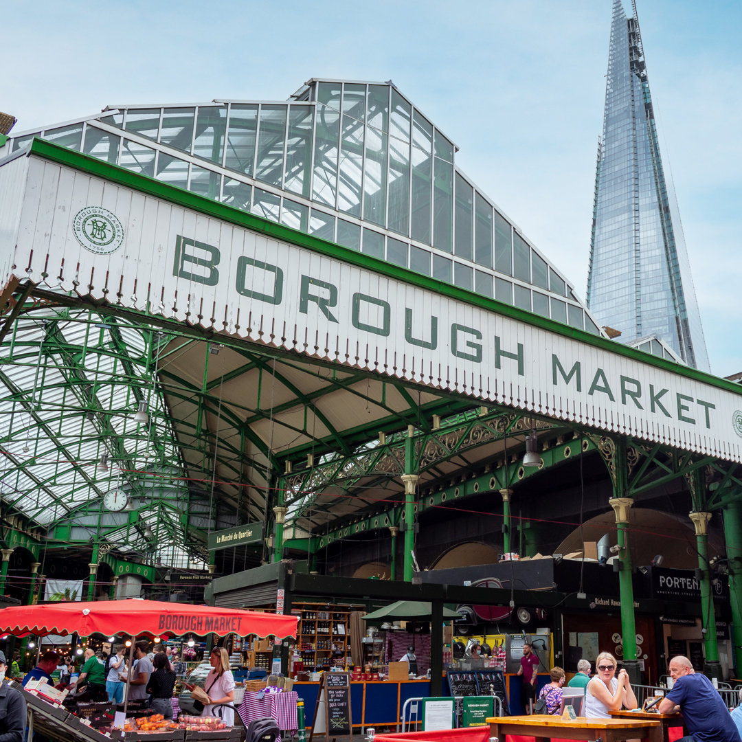 People sit outside stalls underneath covered market with the Shard in the background