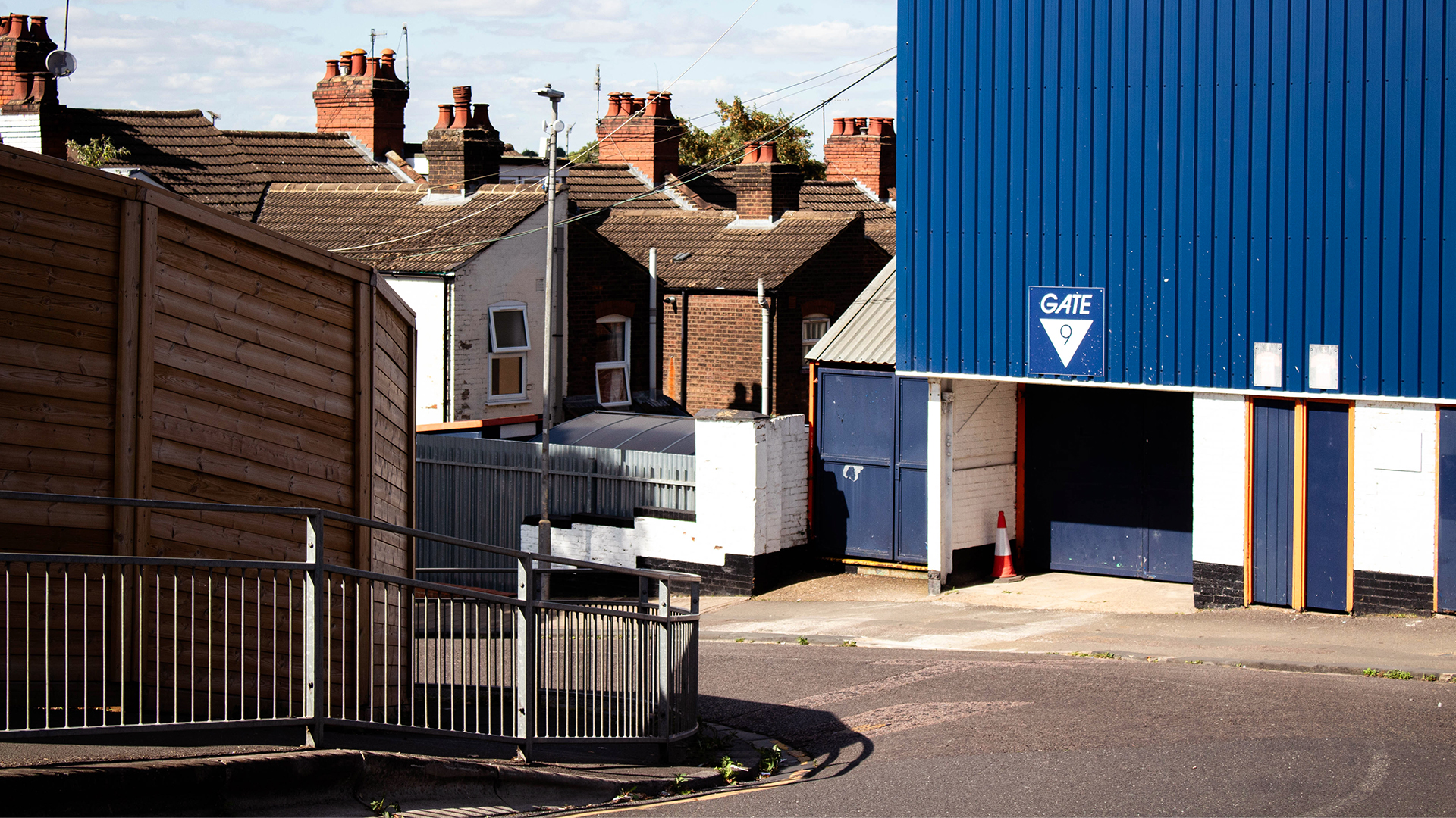 Rooftops of terraced housing next to blue clad stadium on a road bend 