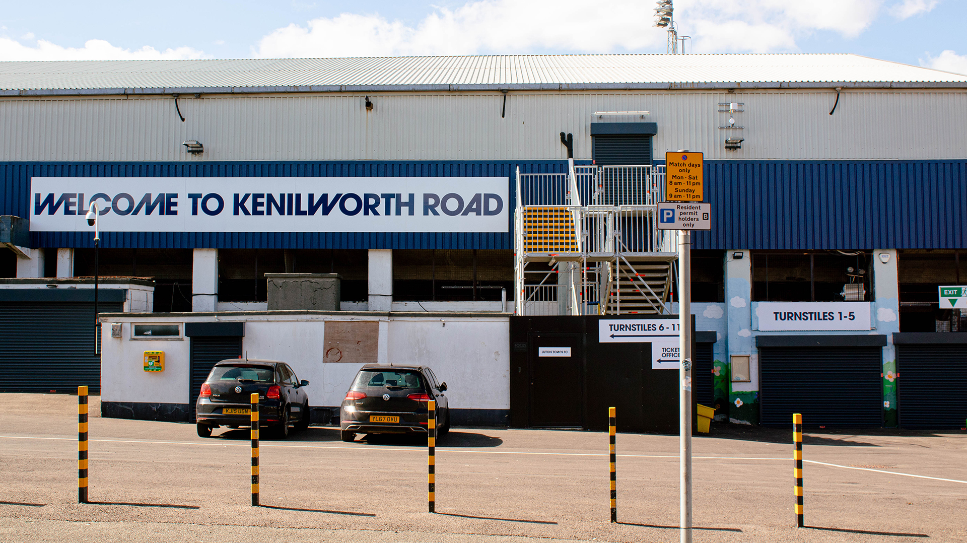 Cars parked outside football stadium with a sign that says welcome to kenilworth road