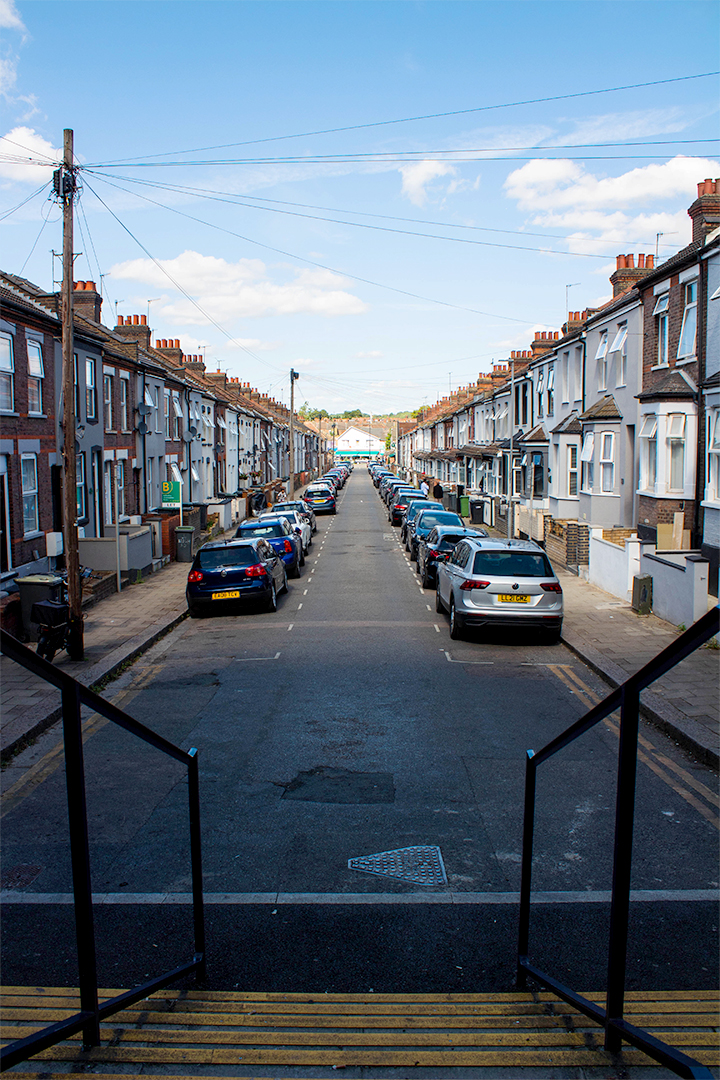 Looking down stairs down a road lined with cars and terraced houses