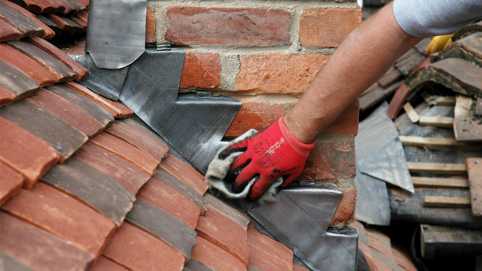 Close up of red tiles on roof and person working on renovation