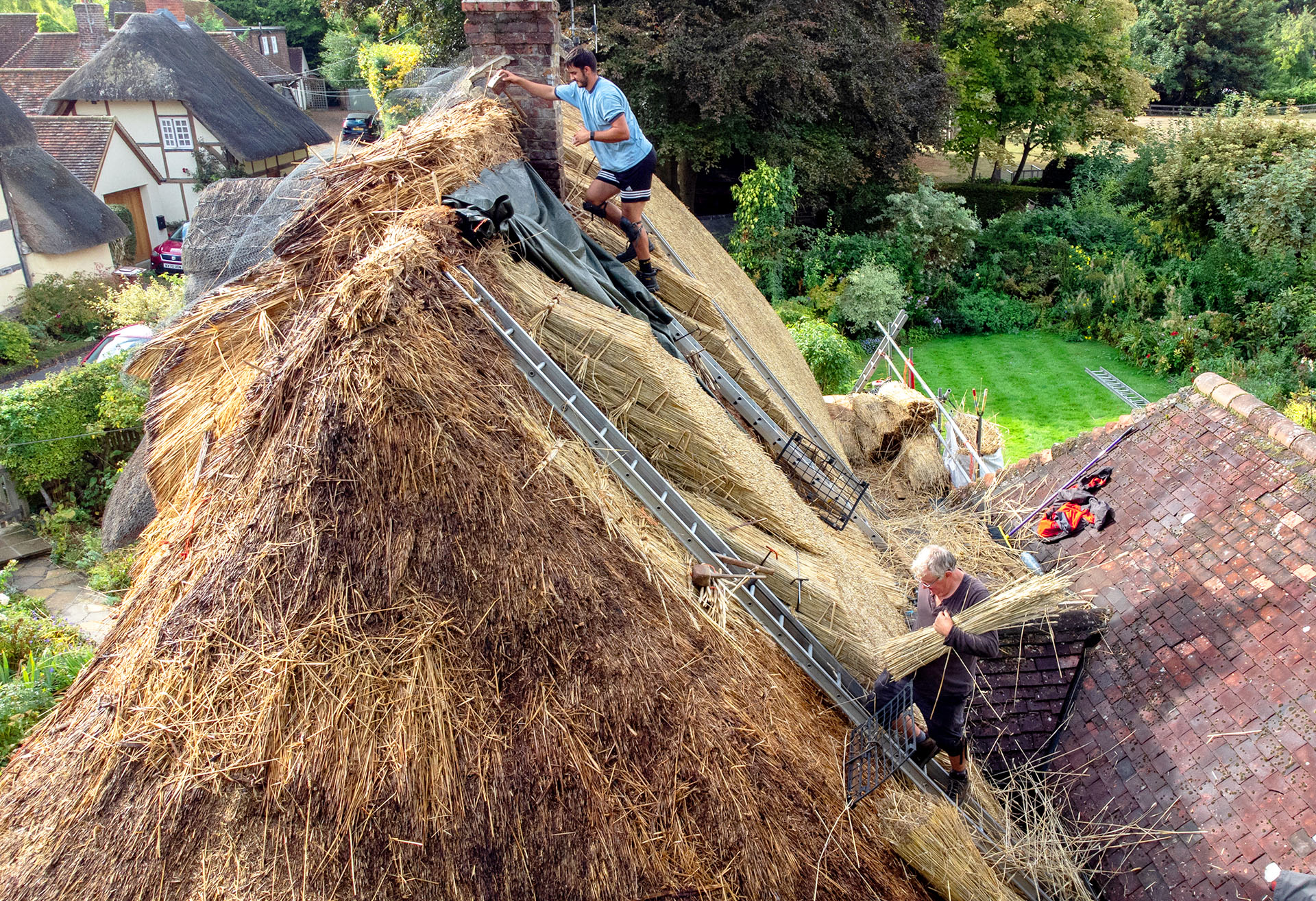 Aerial view of people working on ladders fixing thatched roof of cottage