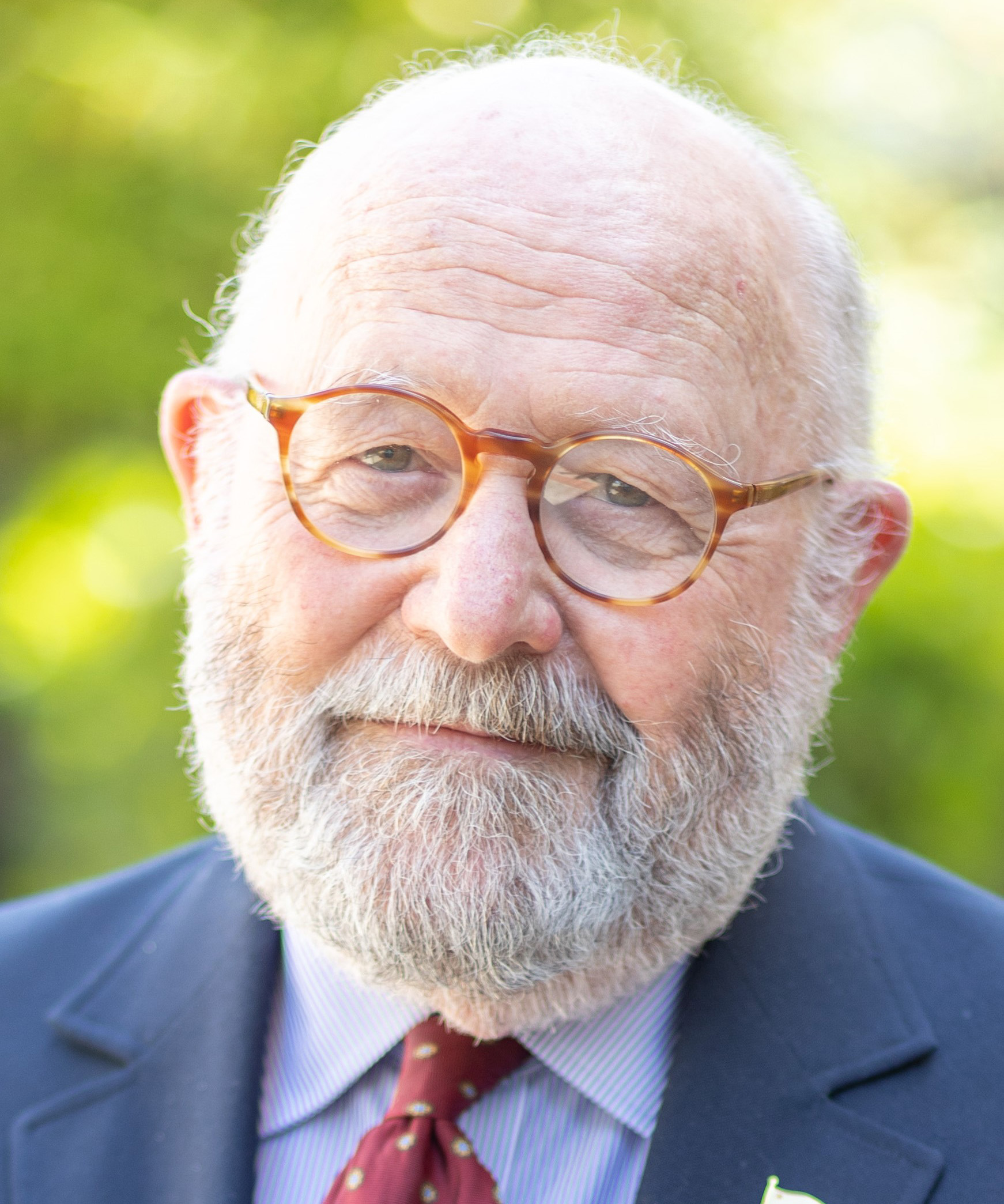 Headshot of Michael Neal Arnold wearing a suit and round glasses, with a blurred outdoor background.