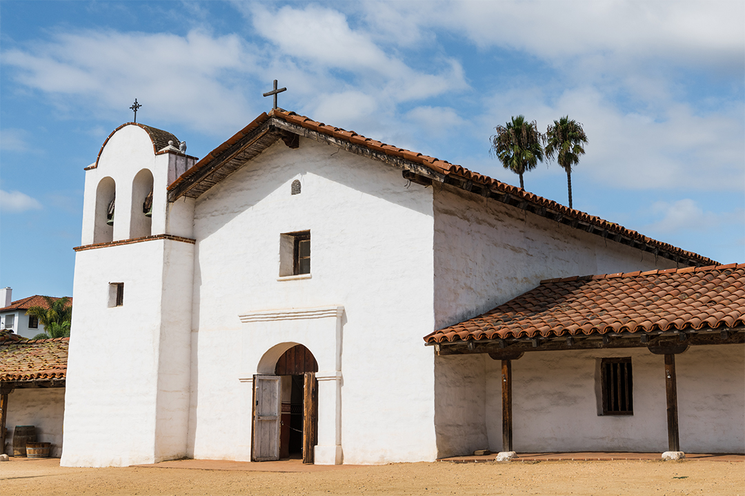 El Presidio de Santa Barbara State Historic Park A white church featuring a striking red roof against a clear blue sky.