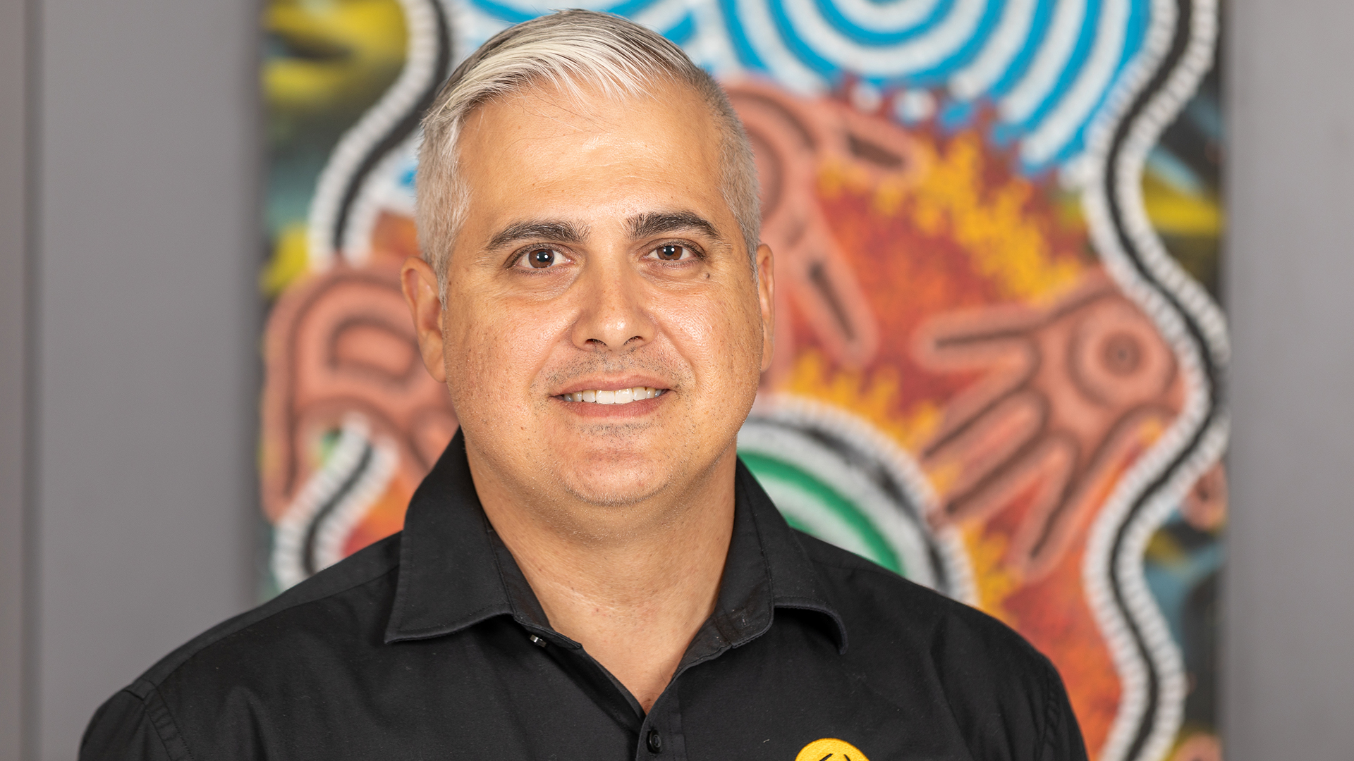 Headshot of Michael Manikas against backdrop of Aboriginal art