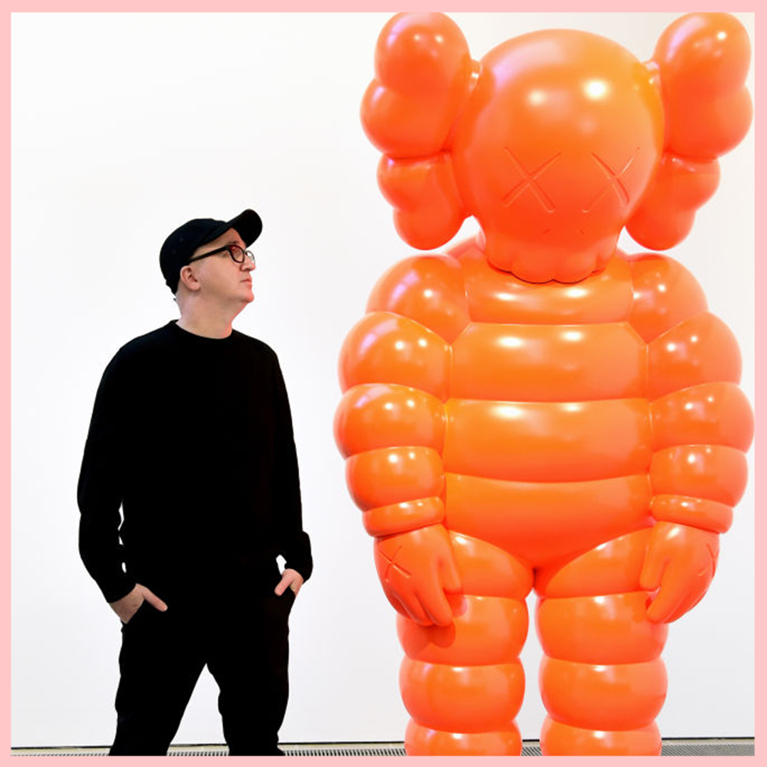 Man in black outfit and black cap stood next to orange sculpture