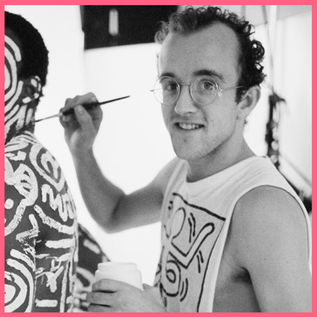 Keith Haring looking to camera whilst painting onto a man's body