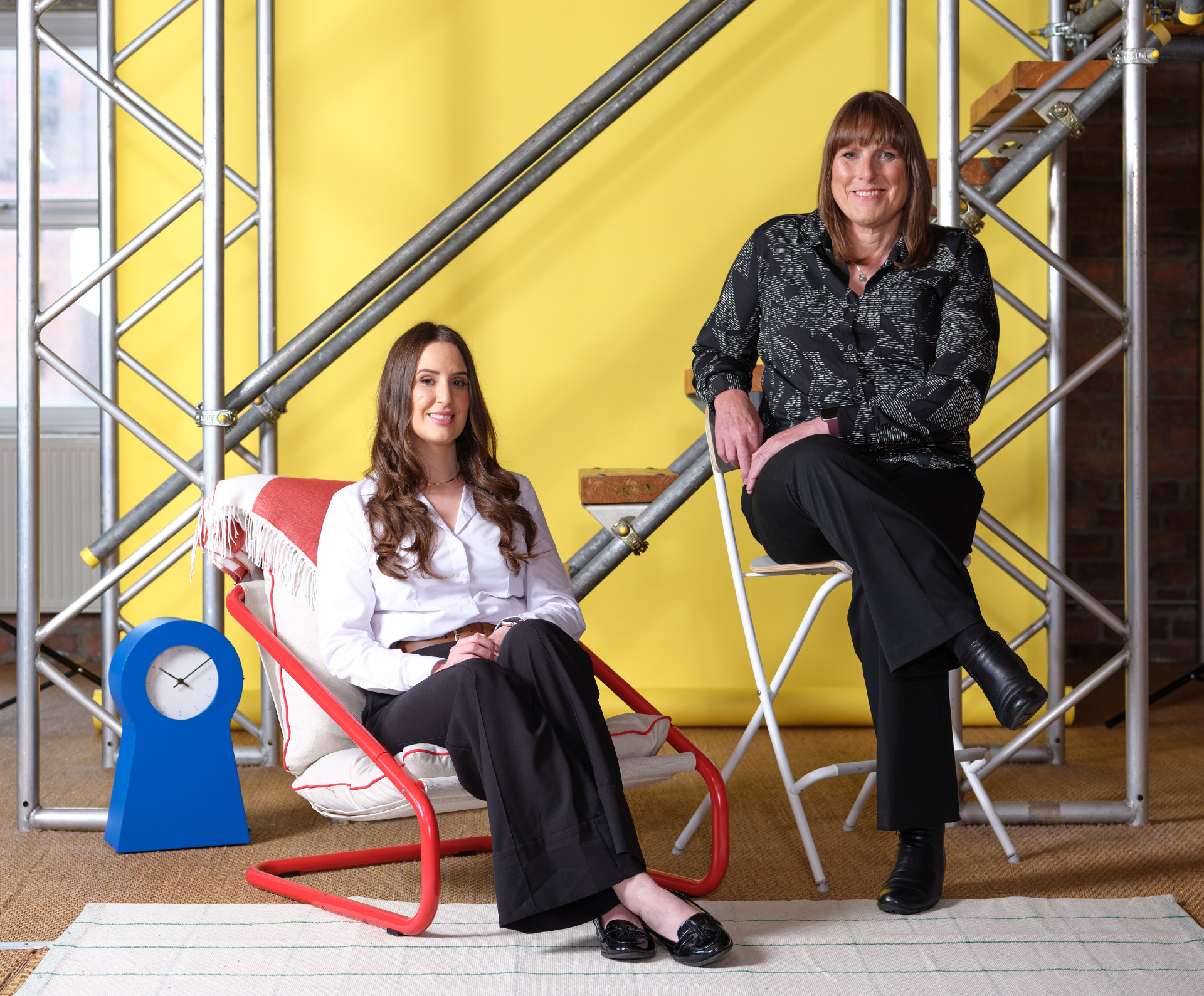 Photos of Louise and Kate Avery sat on chairs with a yellow background and scaffolding