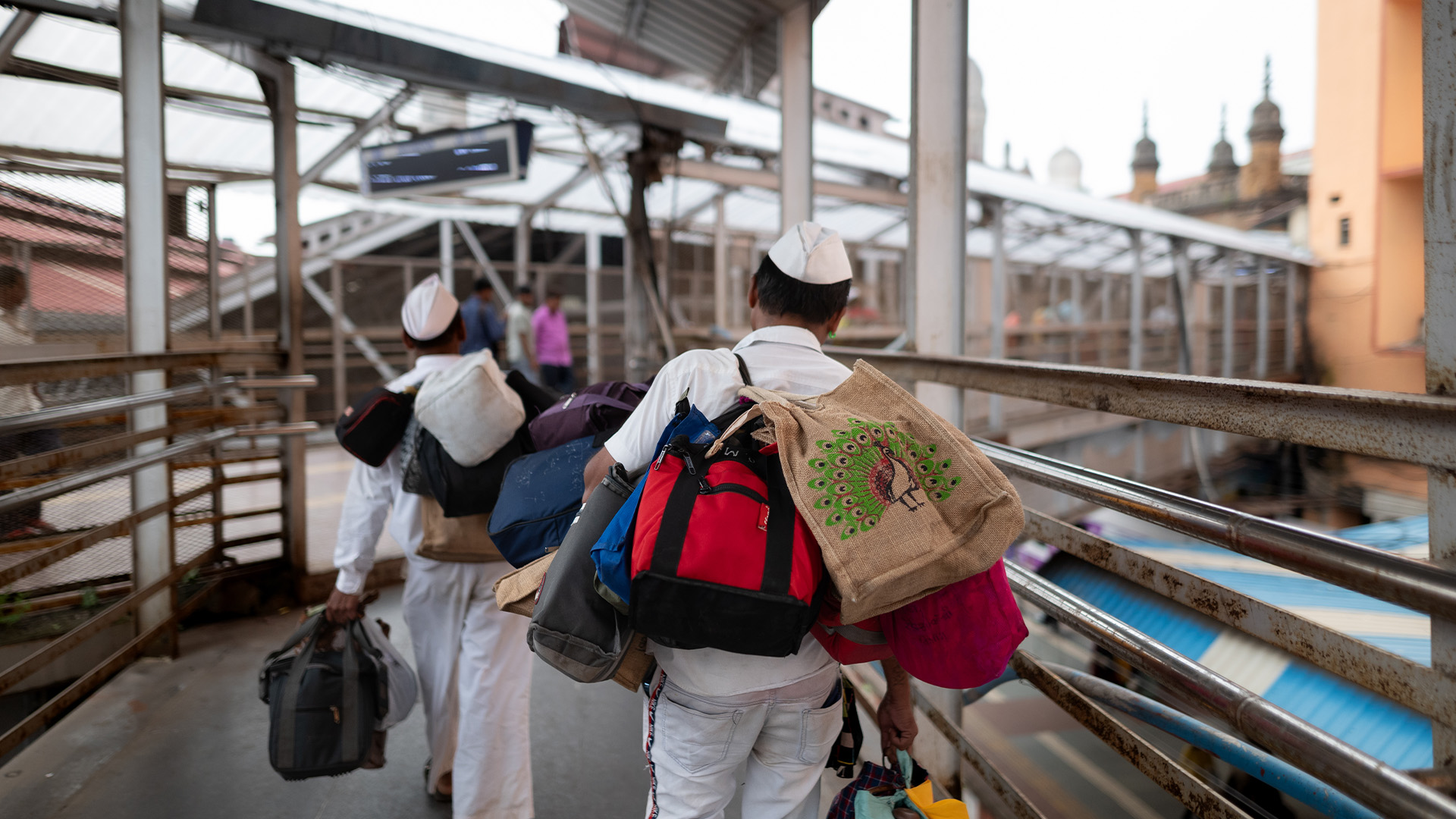 Dabbawalas carry lunch boxes in train station over a bridge