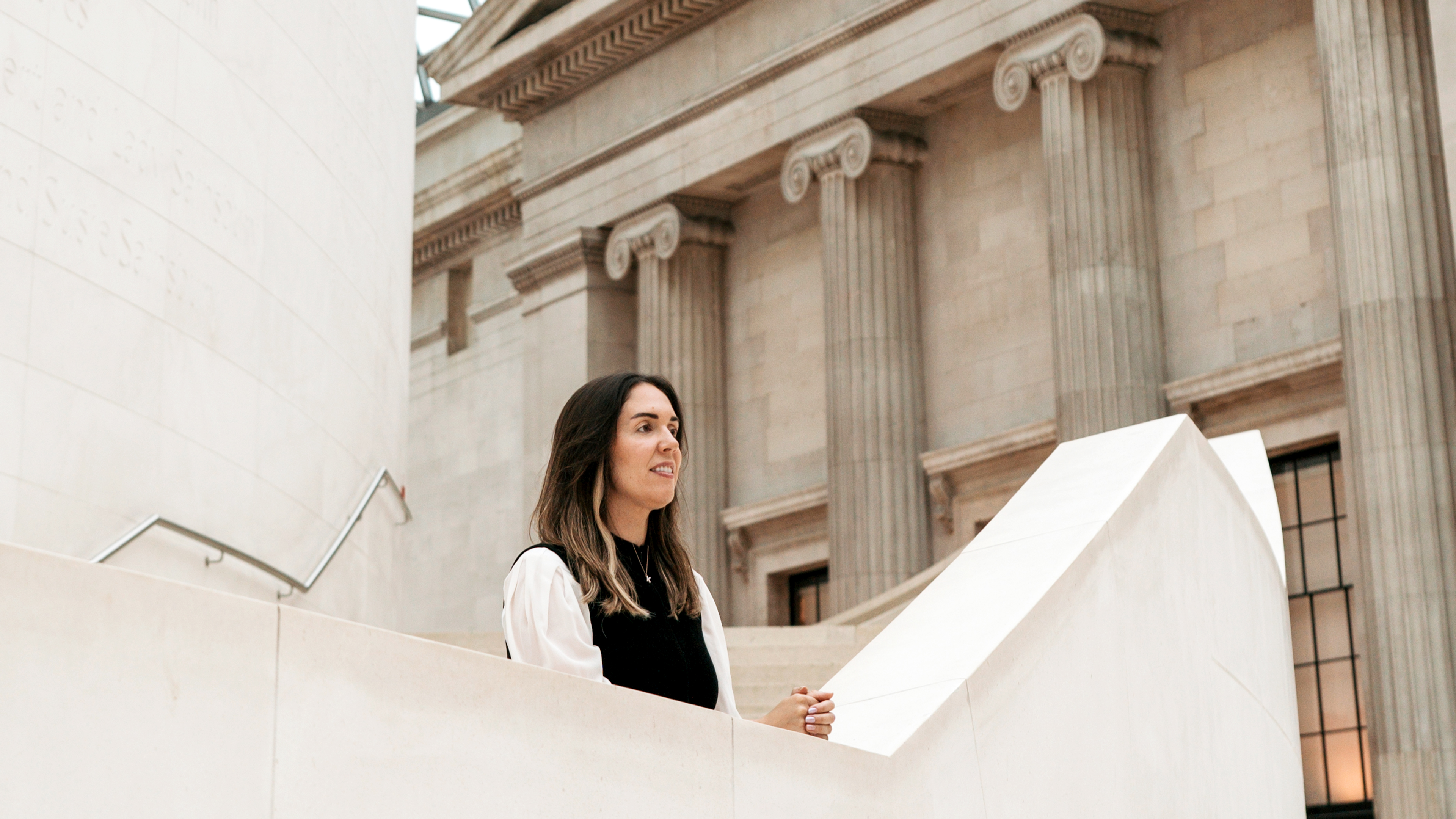 Katharine leans on ledge of marble staircase looking out