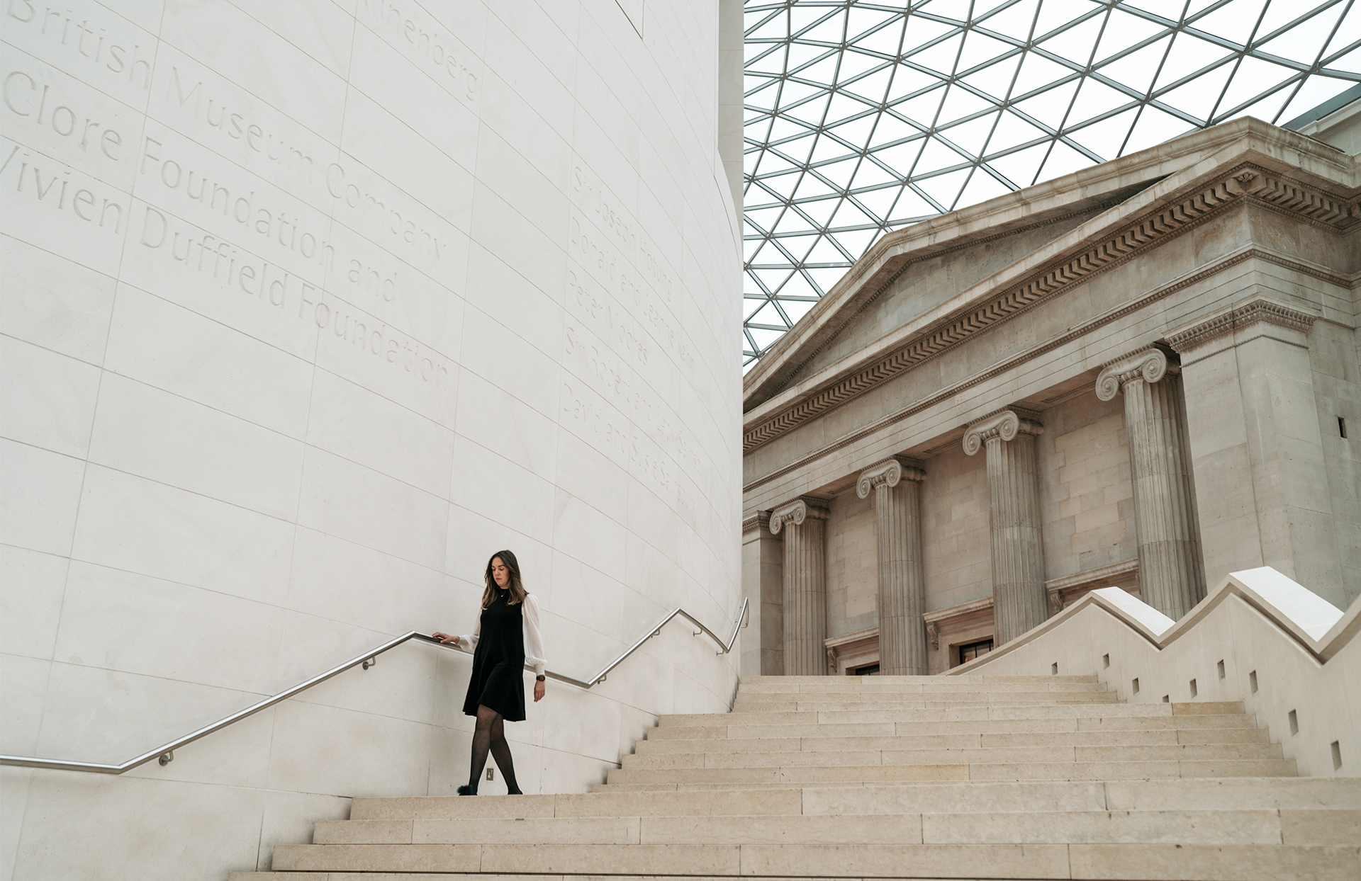 Wide angle of Katharine walking down stairs with old building with greek columns in the background