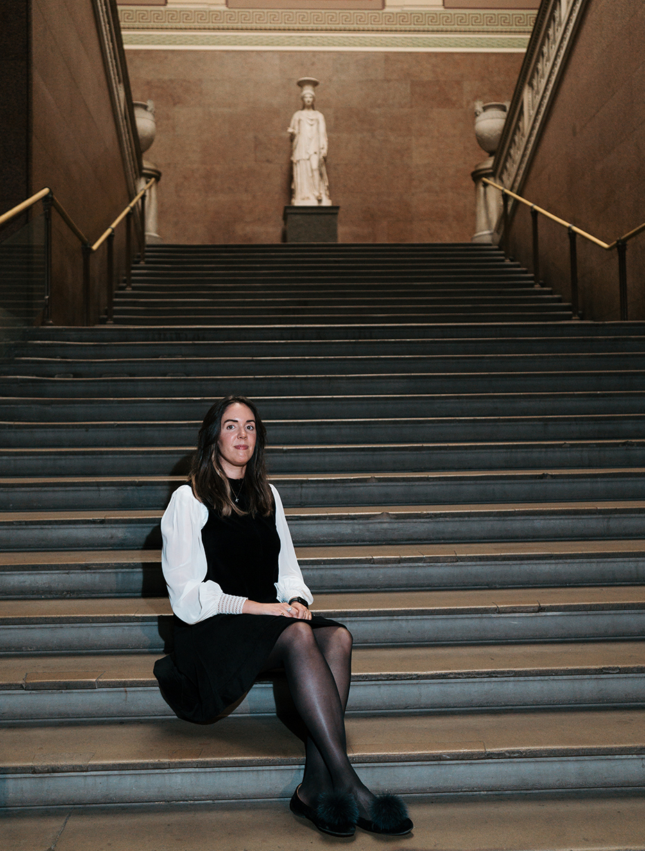 Katharine sits at the bottom of a grand staircase with sculptures at the top of the stairs