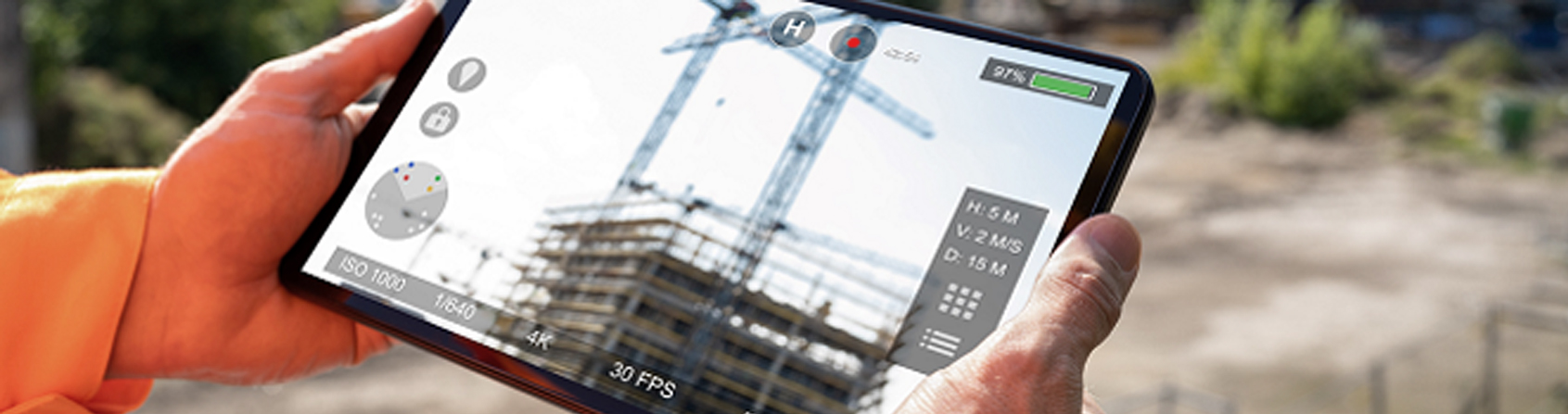 PERSON HOLDING A TABLET WITH A PICTURE OF CRANES CONSTRUCTING A BUILDING