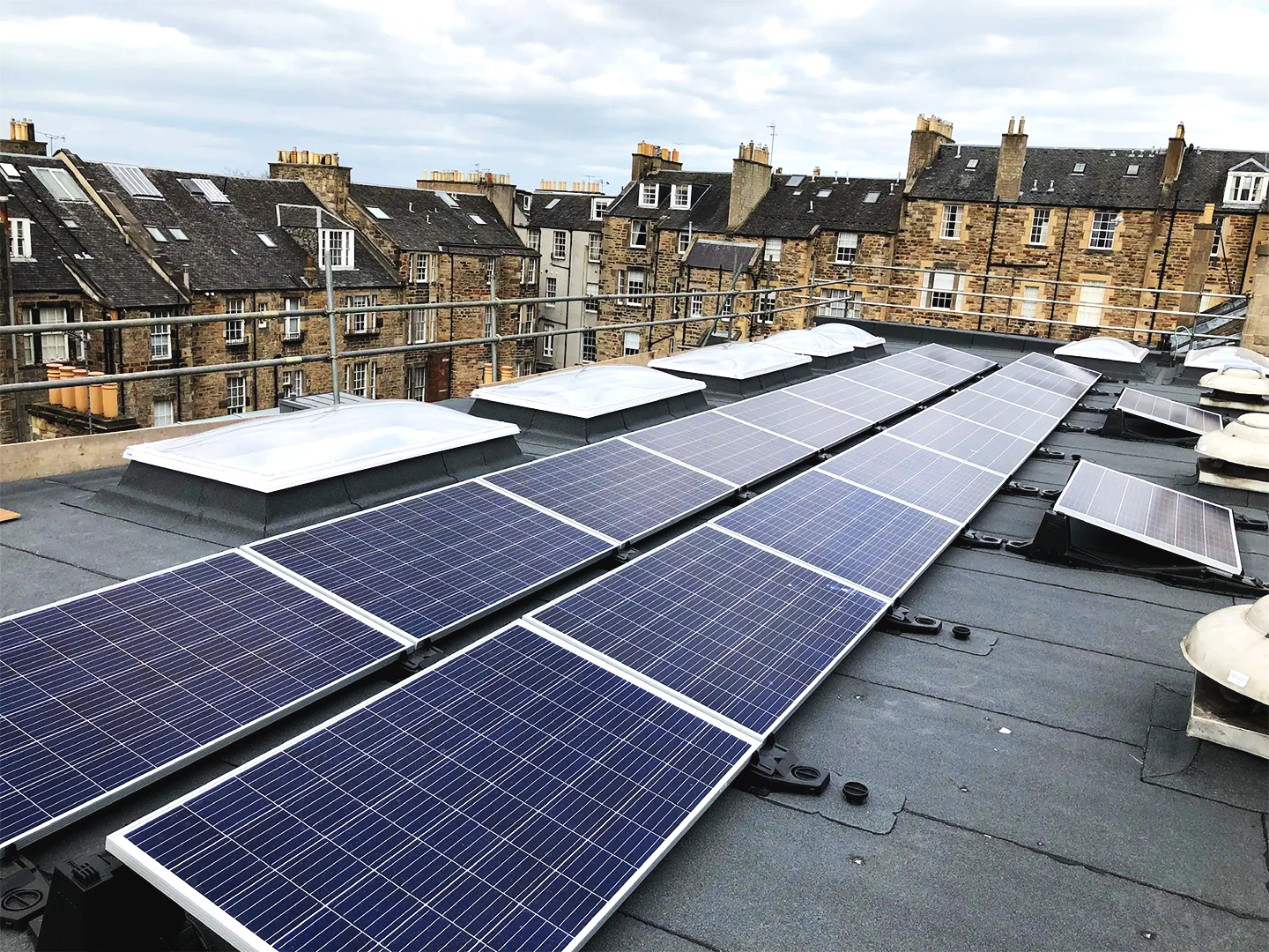 Two lines of solar panels on top of a flat roof overlooking town houses