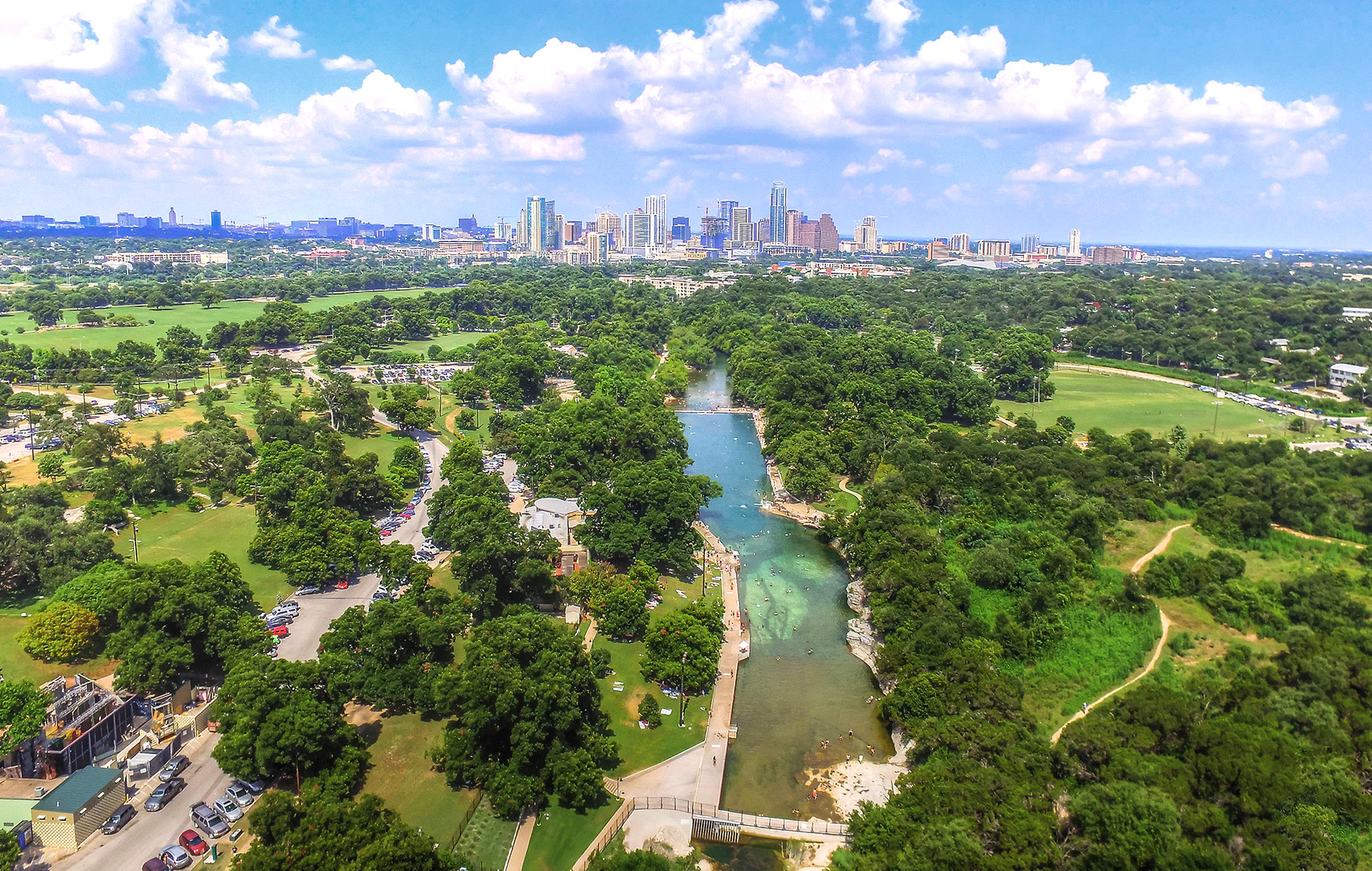 Aerial view of springs surrounded by greenery and view of Austin in the distance