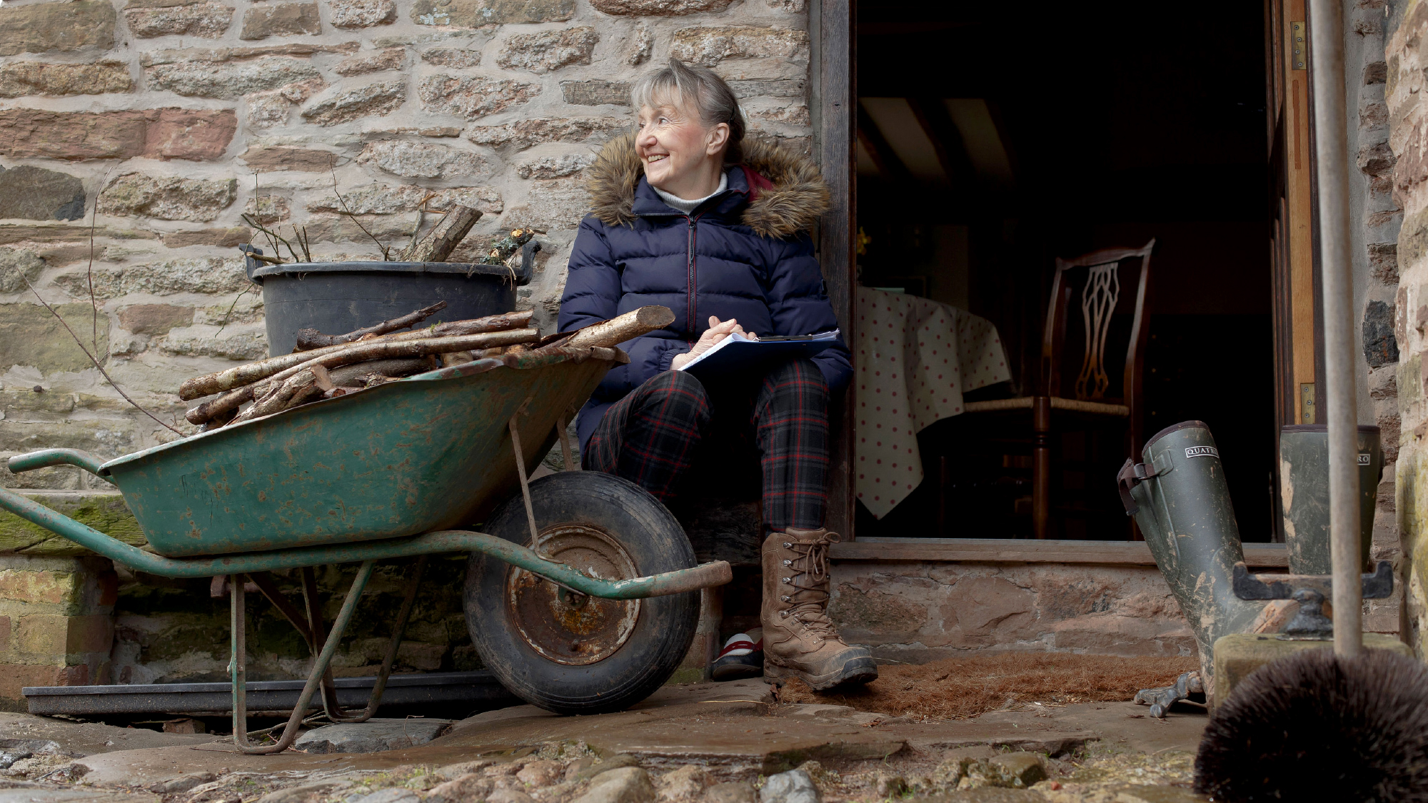 Female farmer sat in front of stone wall next to wheelbarrow