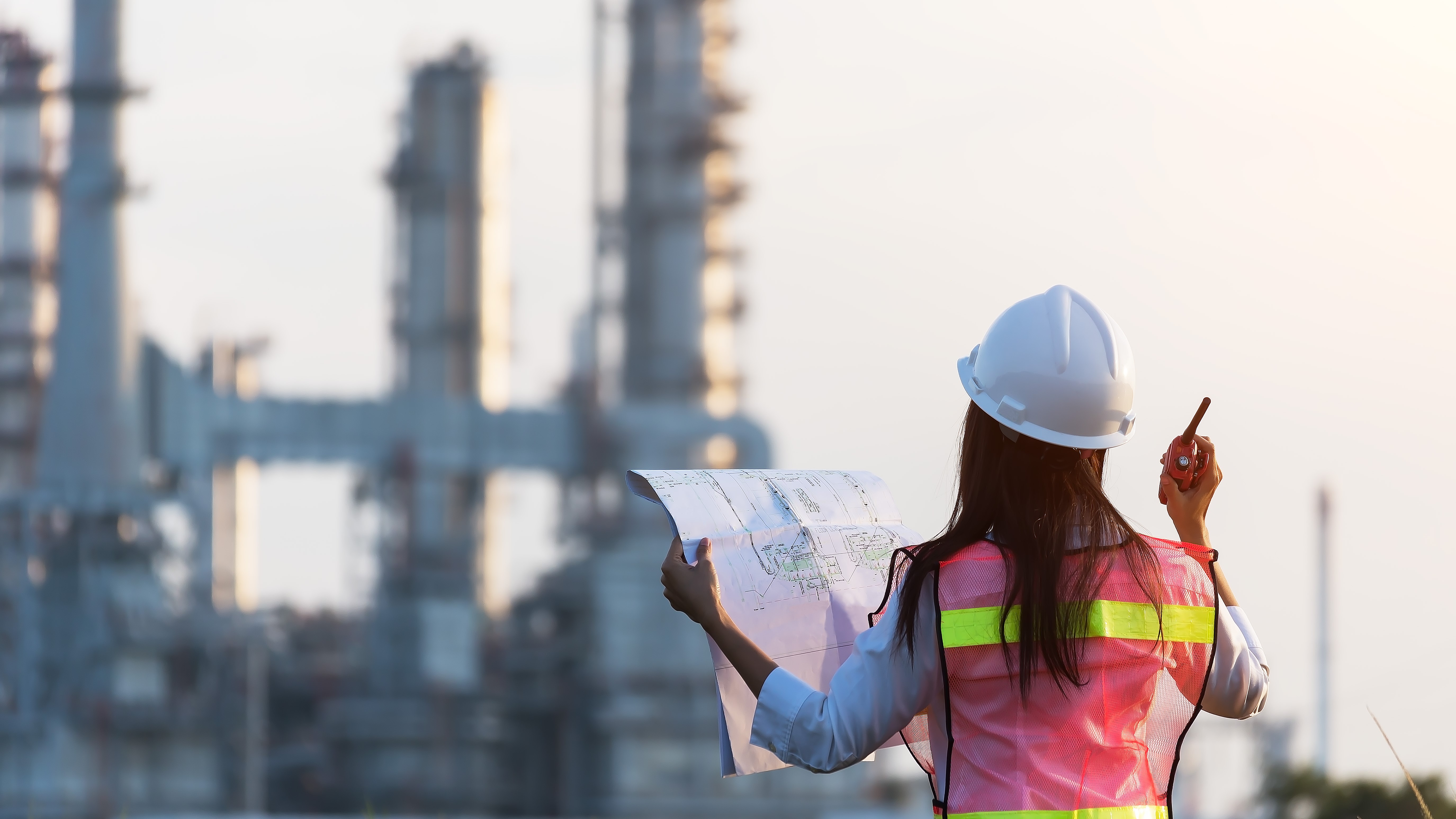 Woman in hard hat in front of industrial site
