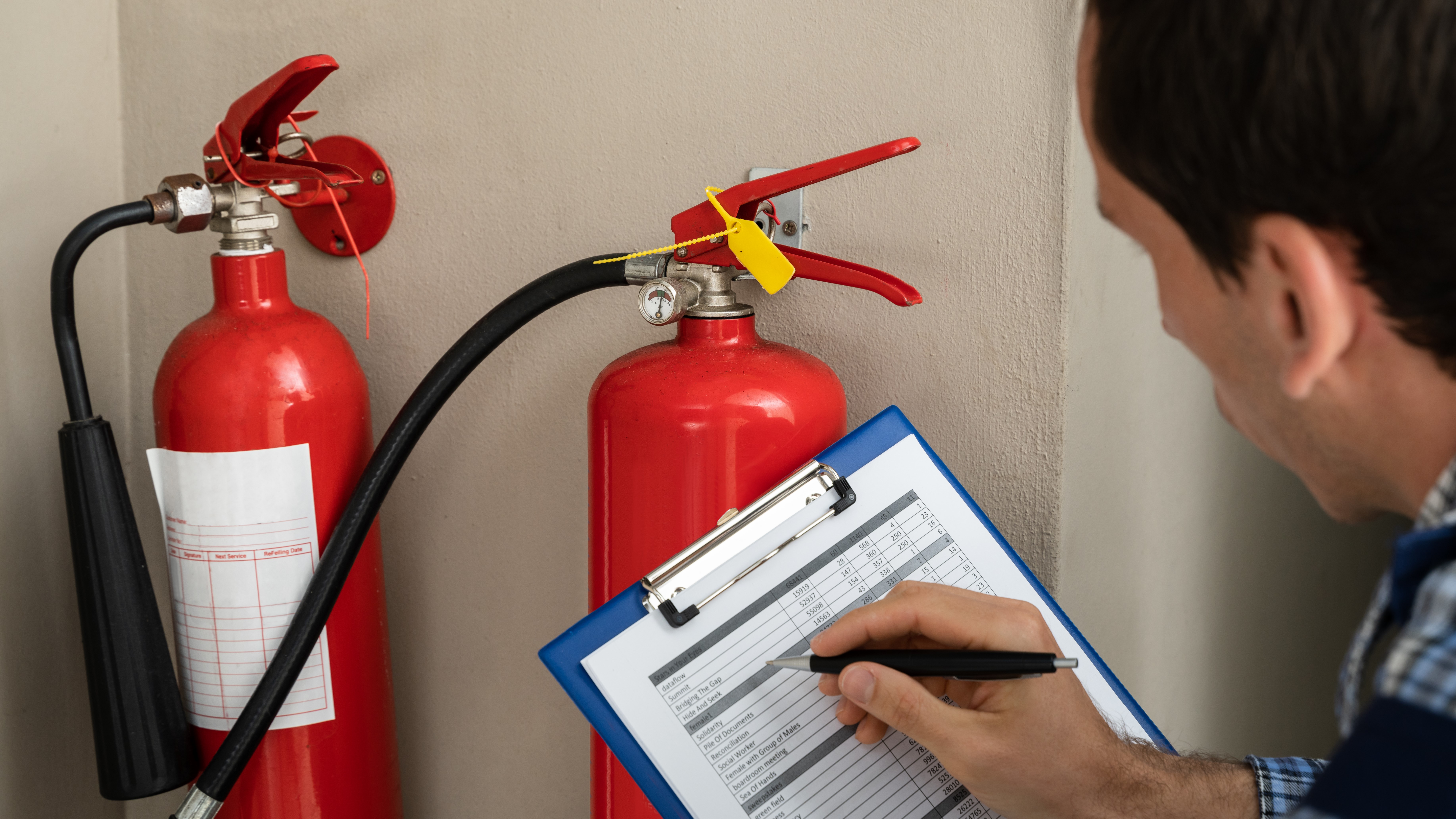 Man holding checklist board next to row of fire extinguishers