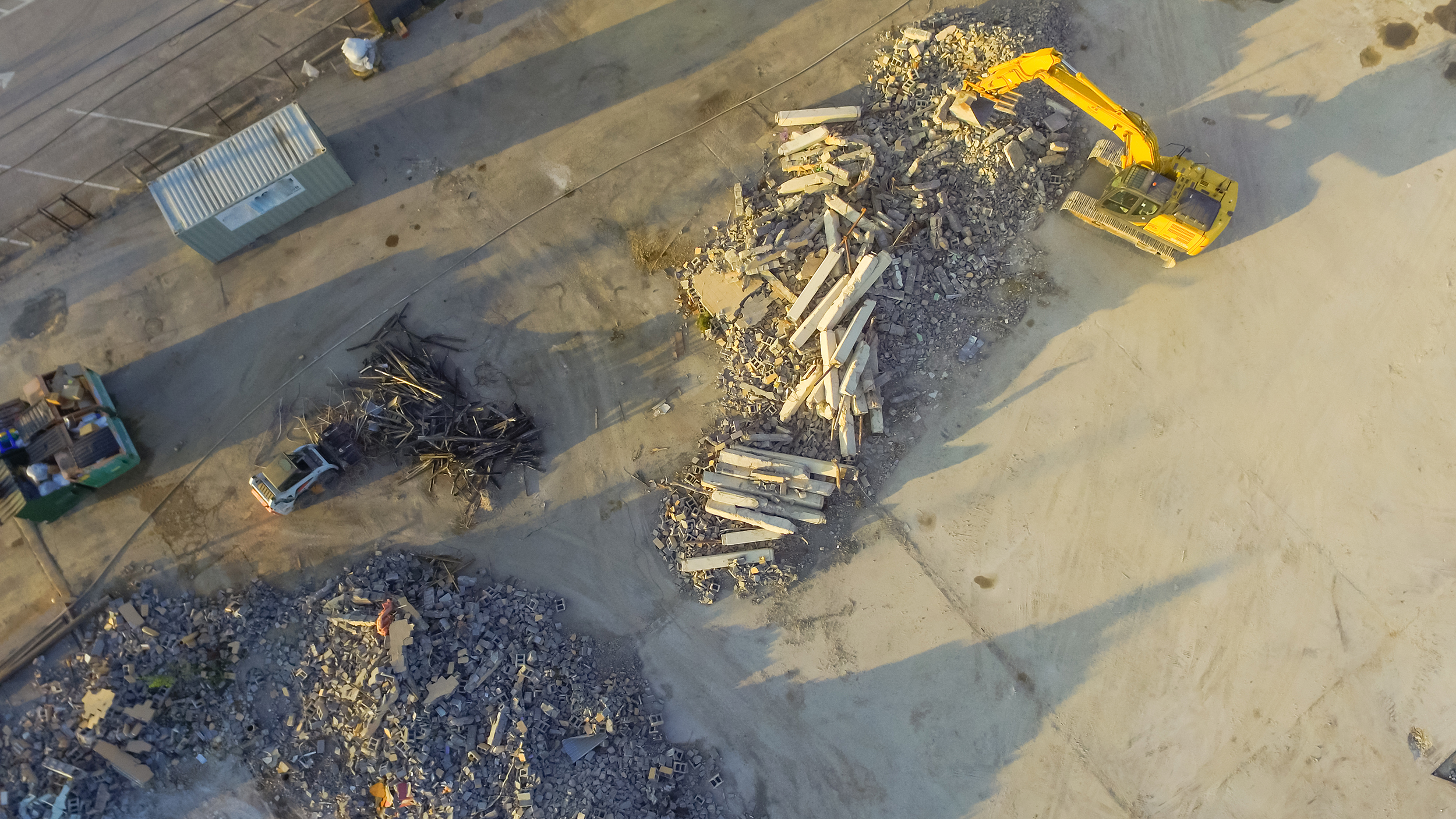Aerial view construction site with rubble and scrap remaining after derelict building demolition. Hydraulic backhoe bulldozer removes crumbling demolished debris, brick, stone and concrete for recycle; Shutterstock ID 466308044; purchase_order: na; job: CJ_July_23; client: ; other: 