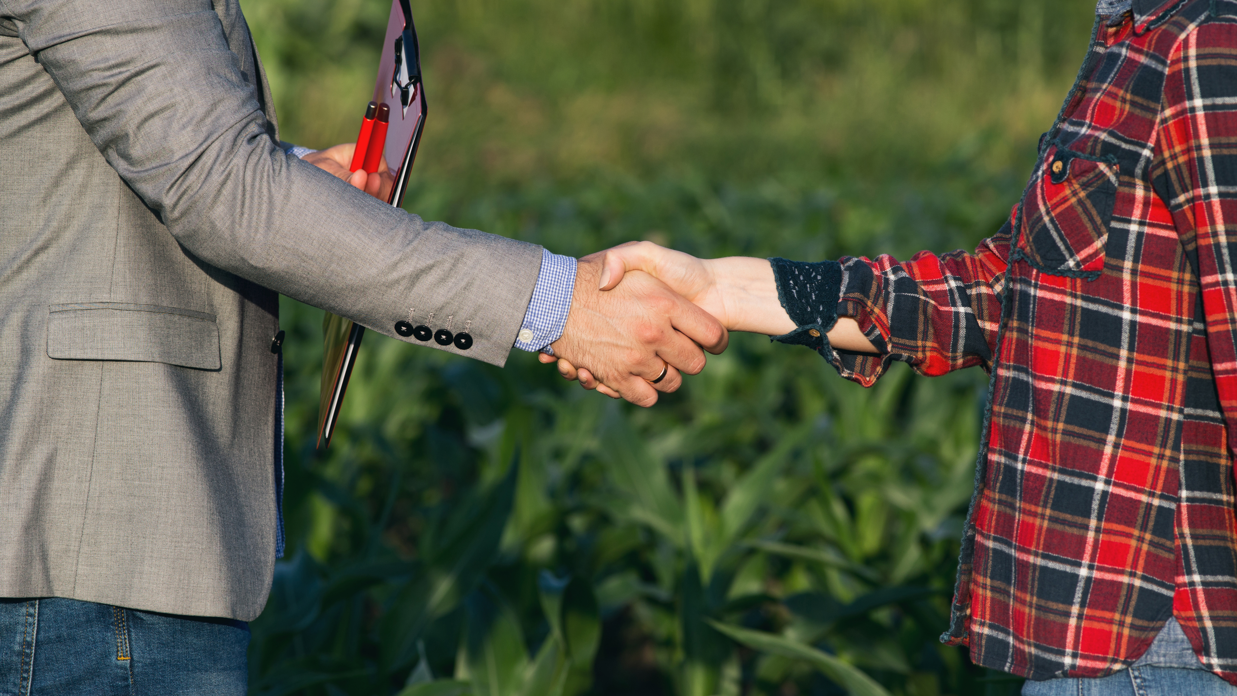 Farmer and business person shake hands with field in background