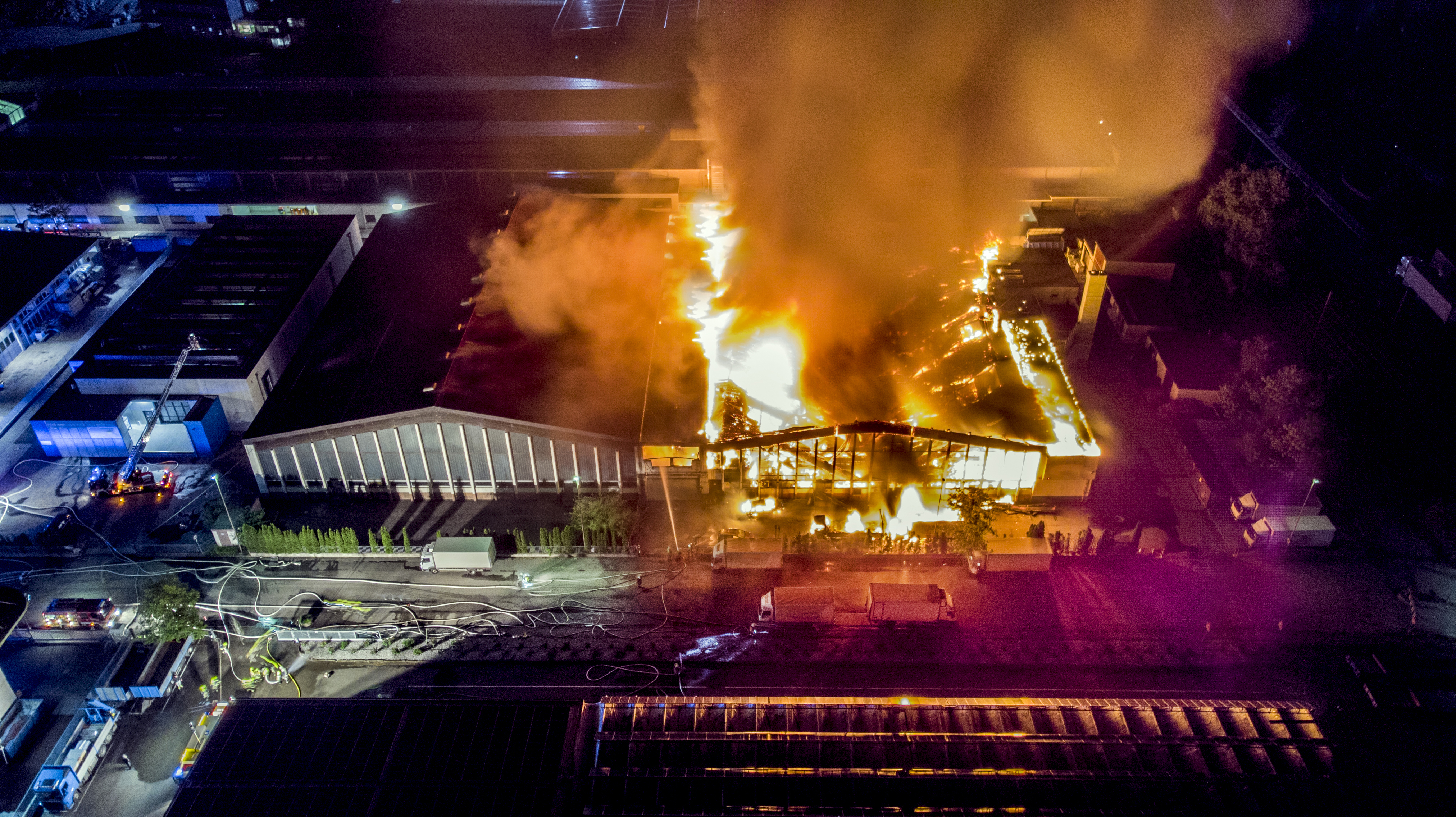 Aerial view a infernal fire in an industrial factory with big flame and smoke above the zone at night. Firemen in action to extinguish the fire in the warehouse zone.; Shutterstock ID 1101013130; purchase_order: NA; job: RICS Property Journal Jan22; client: RICS; other: 
