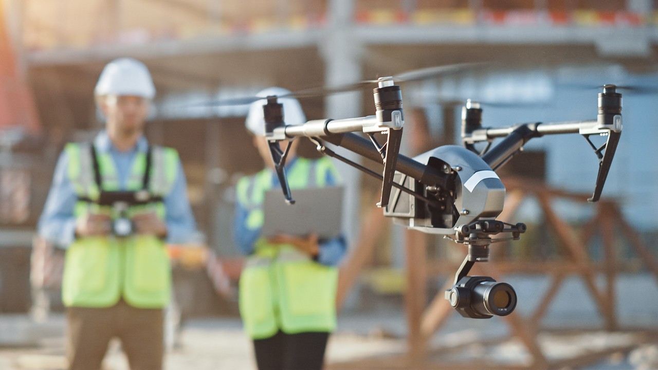 Two men on construction site piloting drone
